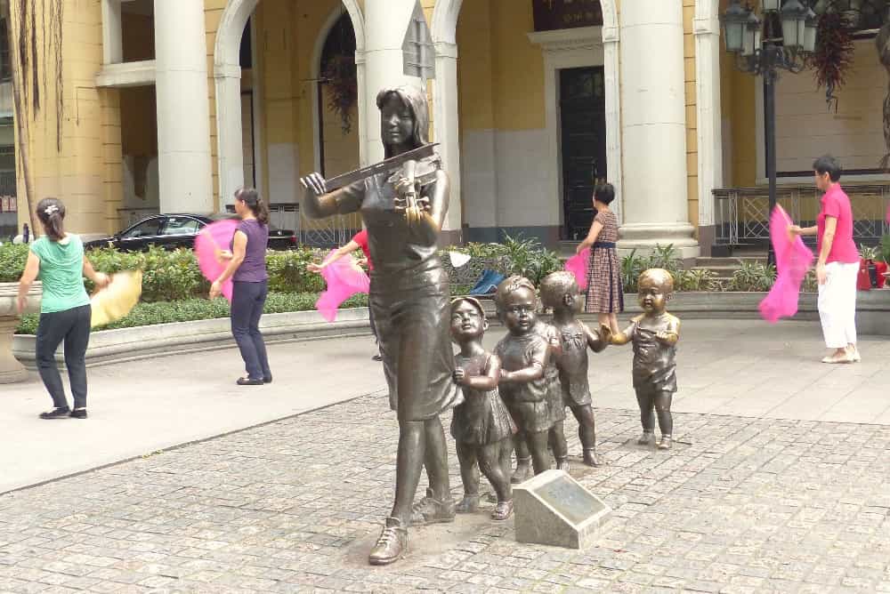 Un groupe de statues de bronze dans le centre ville. A l’arrière-plan, des petits groupes de gymnastique